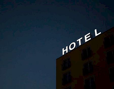 The image shows the top corner of a building with a lit-up sign that reads "HOTEL" against a dark nighttime sky.